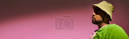 trendy young man with beard in panama posing in profile on pink background, fashion concept, banner