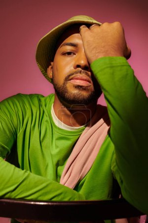 handsome young man with beard in green hat with palm on his face looking at camera, fashion concept
