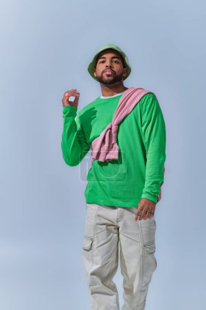 african american man with raised hand looking at camera on light blue backdrop, fashion concept