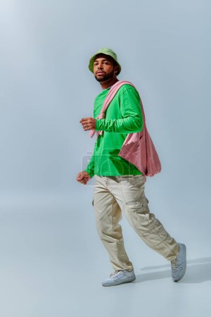 młody stylowy mężczyzna w zielonej bluzie i panama spacery i patrząc w aparat fotograficzny, koncepcja mody