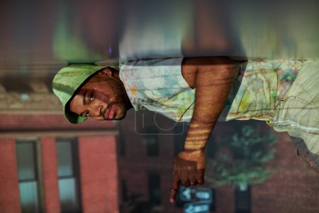 Photo for Trendy african american man in casual attire lying on floor in projector lights, fashion concept - Royalty Free Image