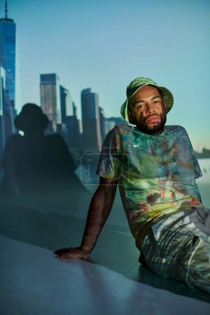 junger afrikanisch-amerikanischer Mann sitzt auf dem Boden und blickt in Projektorlichter auf die Kamera, Modekonzept