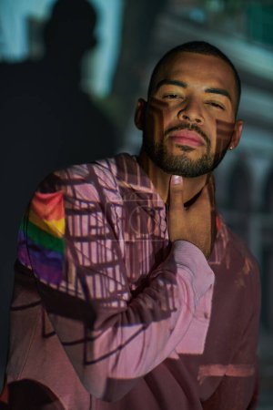 stylischer bärtiger Afroamerikaner, der in digitalen Projektorleuchten auf die Kamera blickt, Modekonzept