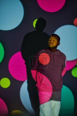 Téléchargez les photos : Modèle masculin afro-américain à la mode avec les yeux fermés dans les projecteurs numériques, concept de mode - en image libre de droit