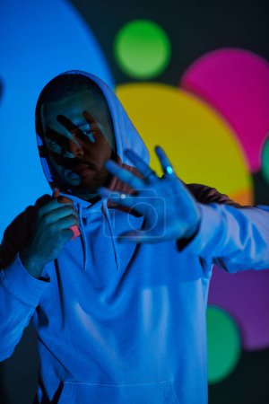 good looking man with hood on putting hand in front of camera in projector lights, fashion concept