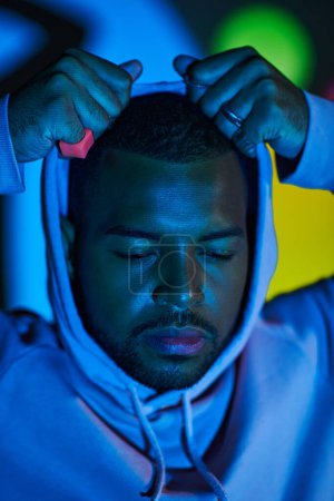 portrait of african american man putting on hood in digital projector lights, fashion concept