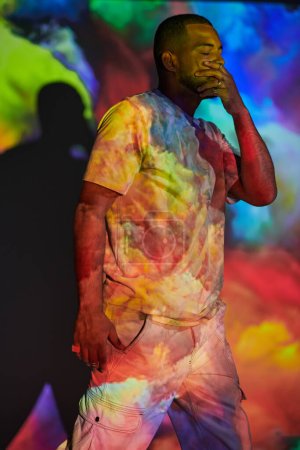 hombre guapo con la mano en la cara en luces brillantes coloridas del proyector digital, concepto de la manera