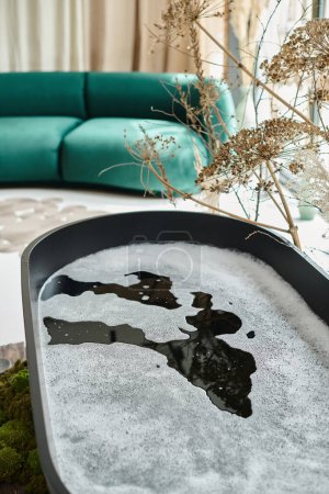 black luxury bathtub with foam in water inside of modern apartment, sofa on blurred background