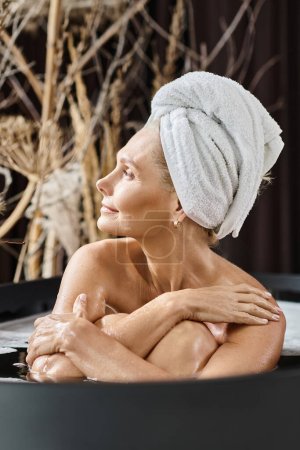 attraktive Frau mittleren Alters mit weißem Handtuch auf dem Kopf badet in moderner Wohnung, Wellnesstag