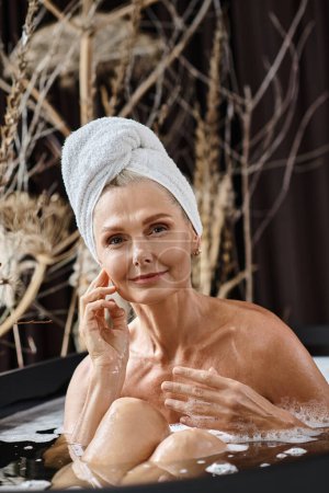 schöne Frau mittleren Alters mit weißem Handtuch auf dem Kopf badet in moderner Wohnung, Wellnesstag