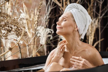 pleased middle aged woman with towel on head and closed eyes taking bath in modern apartment