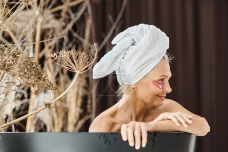 mujer de mediana edad con toalla blanca en la cabeza y bajo los parches de los ojos tomando baño en casa