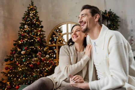 fröhlich verheiratetes Paar, Mann und Frau sitzen neben verschwommenem Weihnachtsbaum, Jahreszeit der Freude