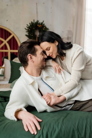 happily married couple lying together on bed near blurred Christmas wreath on wall, season of joy