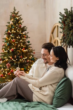 couple marié heureux ayant matin confortable près des lumières floues de l'arbre de Noël sur fond