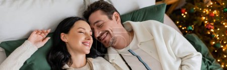 top view of happy married couple spending cozy morning in bed near blurred Christmas tree, banner