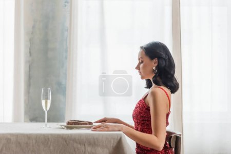 Téléchargez les photos : Vue latérale de la femme élégante en robe rouge assise à table avec verre de champagne et steak - en image libre de droit