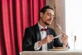 well-dressed man in tuxedo enjoying taste of beef steak near champagne in glass on dining table t-shirt #675984480