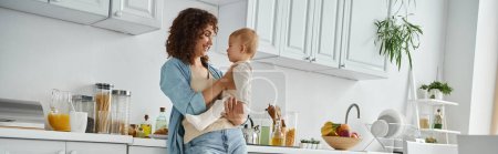 joyful woman standing with adorable toddler daughter in modern spacious kitchen at home, banner