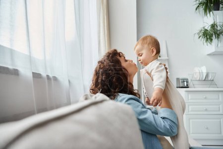 Photo for Side view of loving mother holding cute toddle daughter on couch in living room, quality time - Royalty Free Image