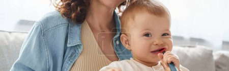 Photo for Toddler girl shewing teething toy and smiling at camera near mother at home, horizontal banner - Royalty Free Image