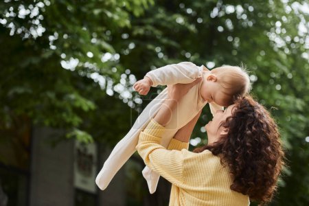 Foto de Feliz madre jugando con un niño pequeño mientras la crían en las manos al aire libre, el ocio y la emoción - Imagen libre de derechos