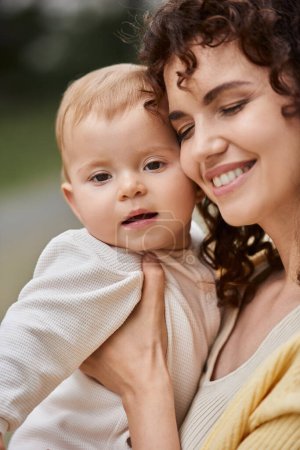 Foto de Retrato de mujer sonriente con los ojos cerrados abrazando niño pequeño al aire libre, momentos felices - Imagen libre de derechos