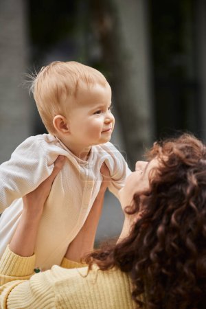 Foto de Mujer con cabello ondulado sosteniendo a la pequeña hija complacida en mamar mientras pasa tiempo al aire libre - Imagen libre de derechos