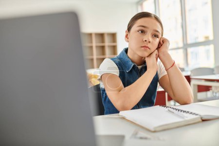 Téléchargez les photos : Une jeune fille absorbée par les pensées à son bureau dans une salle de classe dynamique - en image libre de droit