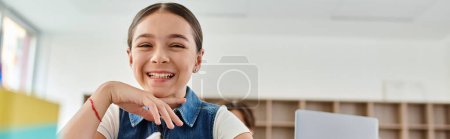Photo for A cheerful girl sits at a desk, smiling brightly as she engages with her surroundings. - Royalty Free Image