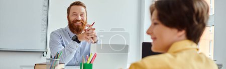 Photo for A man sits at a desk, teaching, while a young boy in front of him listens intently. - Royalty Free Image