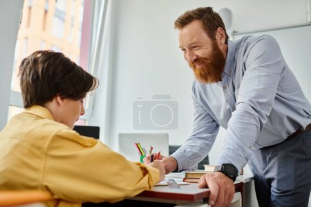 Foto de Un hombre con una barba floreciente está sentado en un escritorio, el niño está absorto en la contemplación y profundo en su estudio. - Imagen libre de derechos