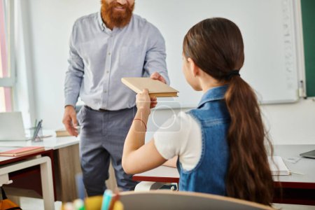 A man teacher stands next to a little girl in a bright, lively classroom, engaged in a conversation or instruction session.