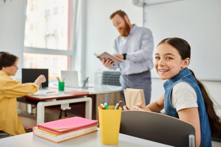 Téléchargez les photos : Une jeune fille engagée dans l'apprentissage, assise à un bureau avec un ordinateur portable ouvert devant, dans un environnement de classe dynamique. - en image libre de droit