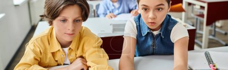 Téléchargez les photos : Un garçon et une fille sont assis à une table dans une salle de classe lumineuse et animée - en image libre de droit