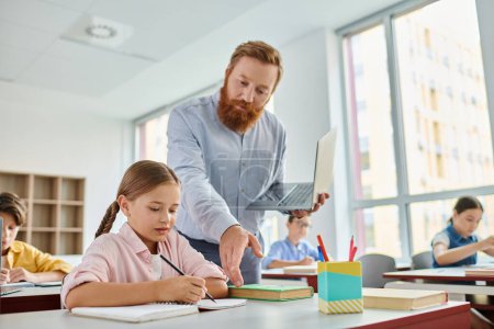 Ein männlicher Lehrer unterstützt ein junges Mädchen bei ihren Hausaufgaben in einem lebhaften Klassenzimmer, umgeben von einer vielfältigen Gruppe engagierter Schüler..