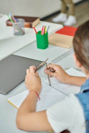 Un niño se sienta en una mesa, sosteniendo la brújula de dibujo en las manos