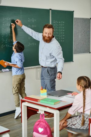 Ein männlicher Lehrer steht selbstbewusst vor einer Tafel und unterrichtet leidenschaftlich eine Gruppe von Kindern in einem hellen, lebendigen Klassenzimmer..