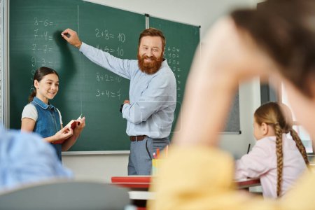 Ein männlicher Lehrer steht vor einer Tafel in einem lebhaften Klassenzimmer und unterrichtet eine Gruppe von Kindern mit Begeisterung und Sachverstand.