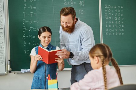 Ein männlicher Lehrer teilt ein Buch mit einem jungen Mädchen in einem bunten Klassenzimmer voller Schüler, die gespannt der Geschichte lauschen.