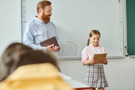 Un hombre está al lado de una niña frente a una pizarra blanca en un ambiente vibrante en el aula, participando en un momento de enseñanza.