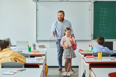 A man teacher stands beside a young girl in a vibrant classroom setting, engaging in interactive teaching.