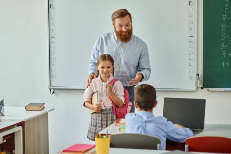 Un profesor de pie junto a una niña en un salón de clases vibrante, discutiendo y participando en actividades educativas con un grupo de niños.