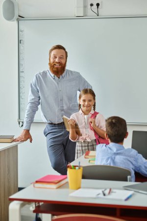 Ein Mann steht vor einem Whiteboard und weist ein kleines Mädchen in ein helles, lebhaftes Klassenzimmer ein, während sie gemeinsam lernen.