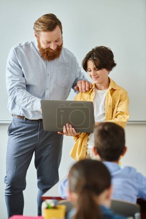 A man and a boy stand together in front of a laptop computer, working collaboratively on a task.