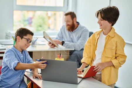 Téléchargez les photos : Un garçon concentré assis à un bureau, s'engageant avec attention avec un ordinateur portable dans un cadre de classe dynamique. - en image libre de droit