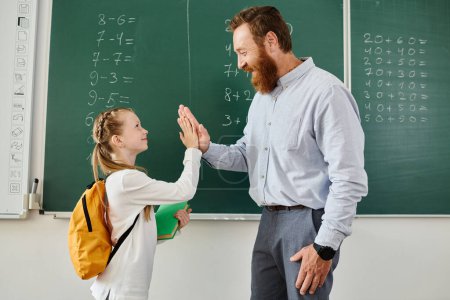 A man and a little girl stand in front of a blackboard, engaged in a teaching moment in a vibrant classroom setting.