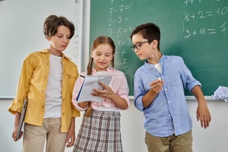 Téléchargez les photos : A group of children stand attentively in front of a blackboard in a vibrant classroom setting. - en image libre de droit