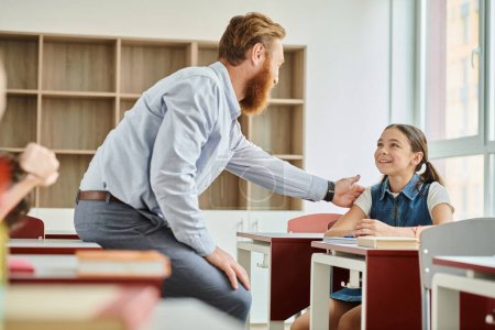 Ein männlicher Lehrer ermutigt ein kleines Mädchen in einem bunten, energiegeladenen Klassenzimmer.
