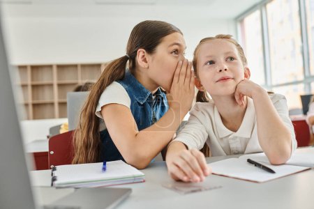 Photo for Two girls sitting at a table, gossiping lively classroom. - Royalty Free Image